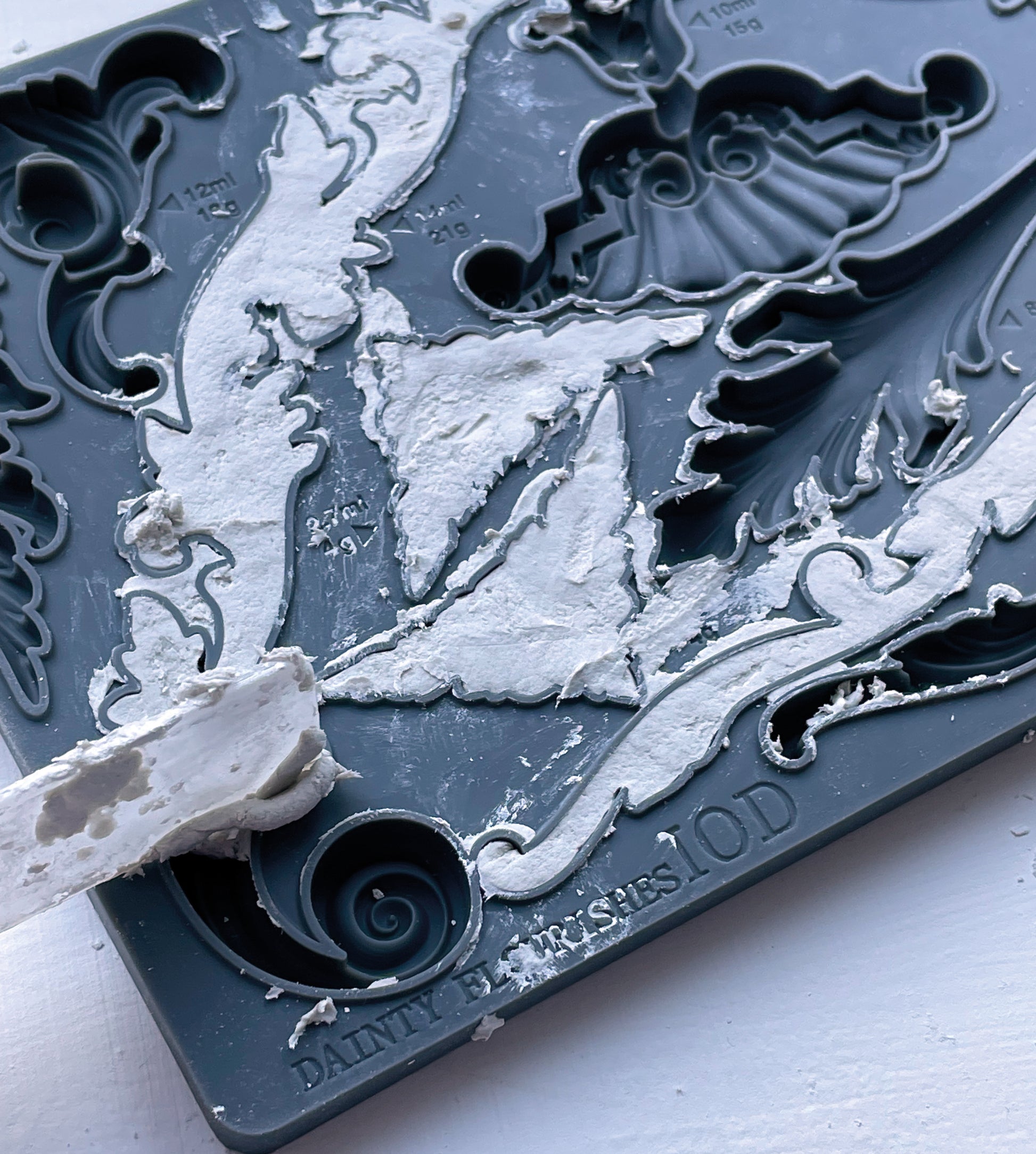 IOD Dainty Flourishes Mould in use — white casting medium being spread into dark grey silicone mould