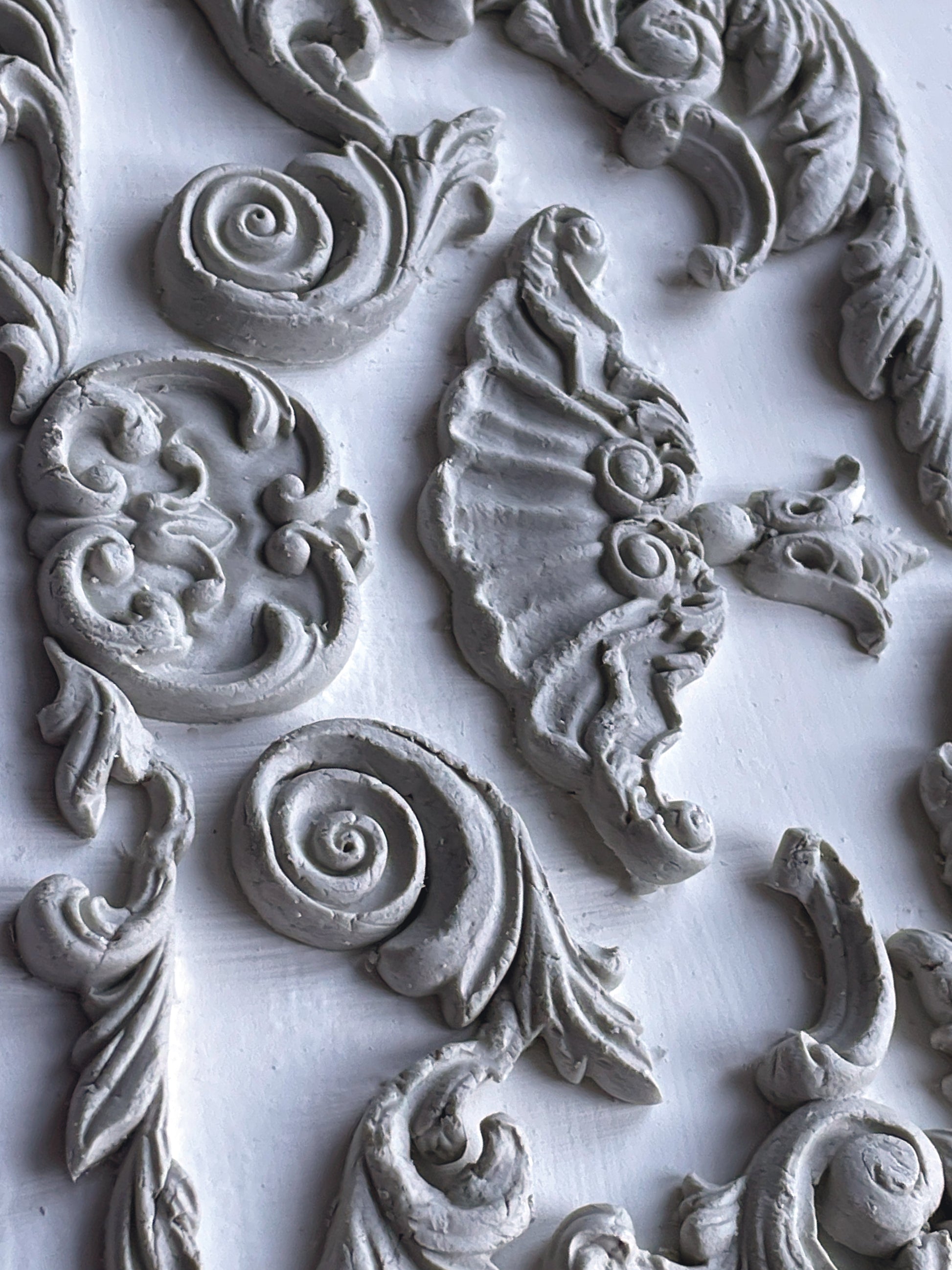 Finished castings from IOD Dainty Flourishes Mould — baroque scrolls, acanthus leaves, shell and spiral motifs in grey clay